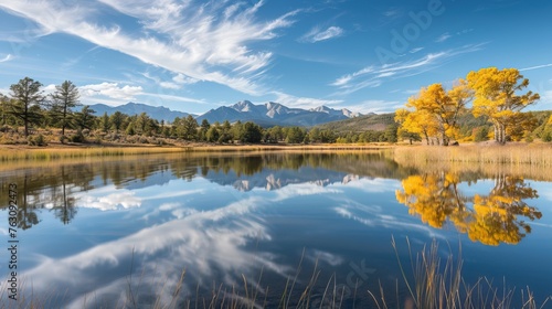 Tranquil autumn landscape with a reflective lake, golden foliage on trees, and a mountain backdrop under a clear blue sky.