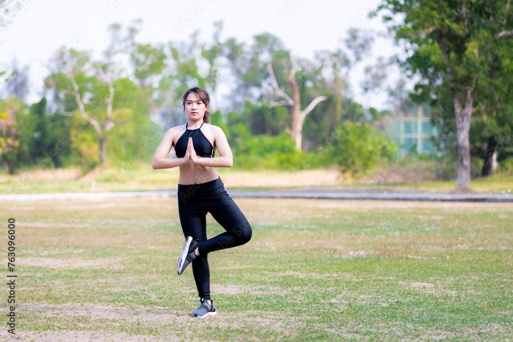Portrait of a young Asian woman standing and exercising in nature, During the summer or spring time. Working women are doing yoga to stretch their legs and muscles. Empty space for entering text. Portrait of a young Asian woman standing and exercising in nature, During the summer or spring time. Working women are doing yoga to stretch their legs and muscles. Empty space for entering text.
