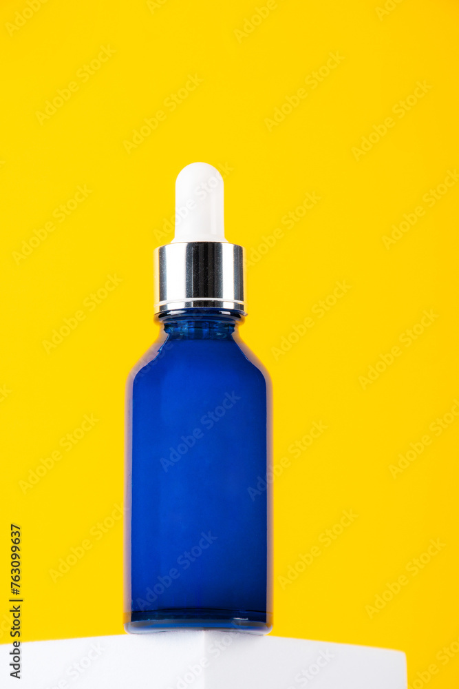 Blue glass cosmetic bottle, Skin care or sunscreen cosmetic with stylish props on yellow and white background.