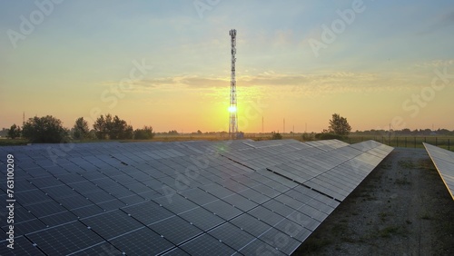 Photovoltaic solar panels at solar farm during golden hour with 5G telecom tower in the background