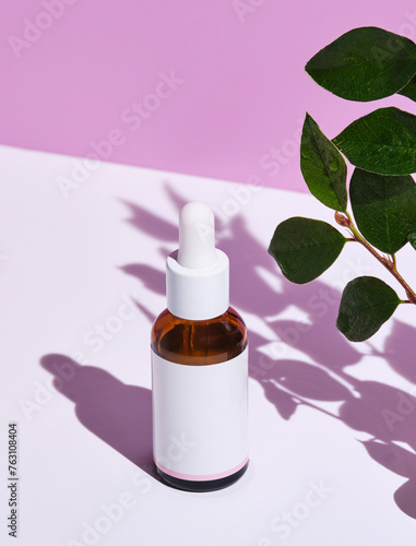 minimalist image showcasing a skincare essence bottle beside fresh green leaves on a dual-tone background.