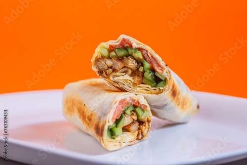 Chicken bacon ranch wrap cut in half on a white plate. Studio shot with orange background. Healthy eating and fast food alternative concept. Design for menu, poster, and banner.