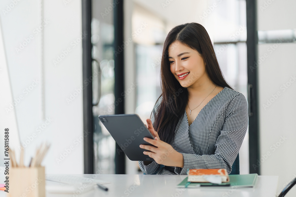 Asian professional businesswoman working on a tablet and desktop computer in a corporate office. Asian professional businesswoman working on a tablet and desktop computer in a corporate office.