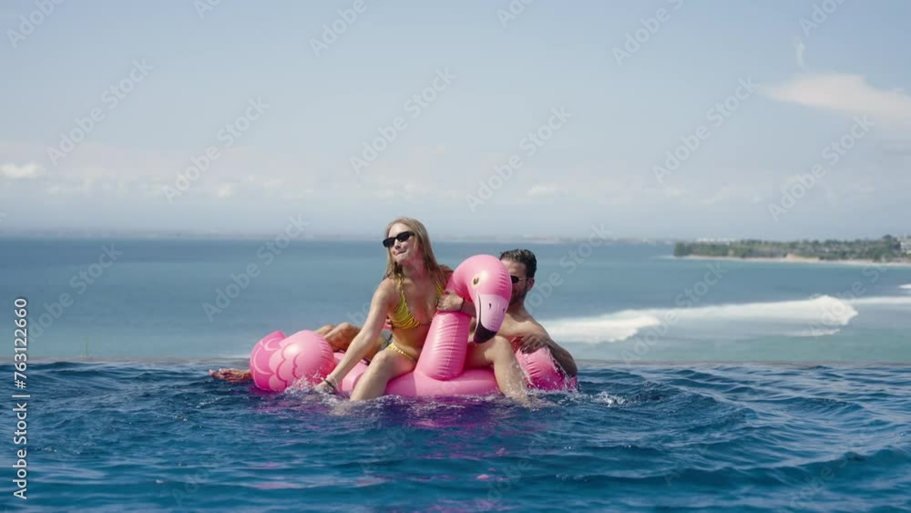 Timelapse of young lover couple swim in infinity ocean view pool with inflatable pink flamingo with splash. Happy memories of honeymoon vacation, friend summer travel together, have fun enjoy Timelapse of young lover couple swim in infinity ocean view pool with inflatable pink flamingo with splash. Happy memories of honeymoon vacation, friend summer travel together, have fun enjoy