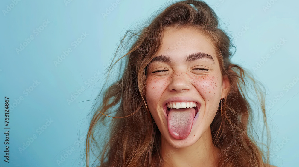 Beautiful girl showing tongue and winking on pastel blue background Beautiful girl showing tongue and winking on pastel blue background