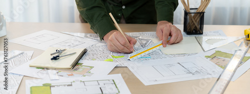 A portrait of architect using divider to measure blueprint. Architect designing house construction on a table at studio, with architectural equipment scattered around. Focus on hand. Delineation © Summit Art Creations
