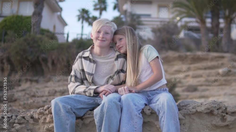 A boy and girl share a smile while sitting on a rock in a natural landscape A boy and girl share a smile while sitting on a rock in a natural landscape
