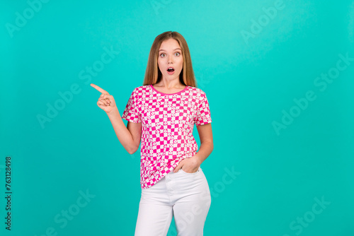 Photo portrait of lovely teen lady point shocked empty space dressed stylish pink print garment isolated on aquamarine color background