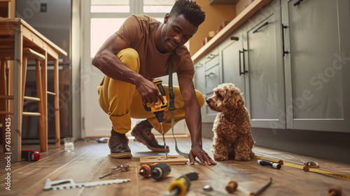 A person kneels to drill a piece of wood as a curious dog watches on. photo