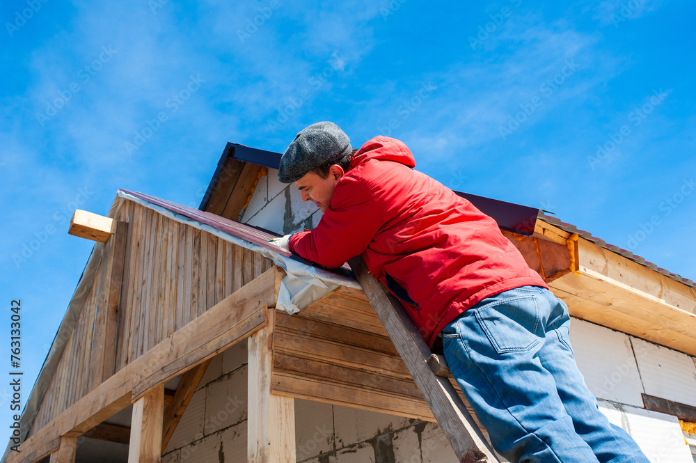 A worker builds a roof in a house while standing on a wooden ladder. Blue sky A worker builds a roof in a house while standing on a wooden ladder. Blue sky