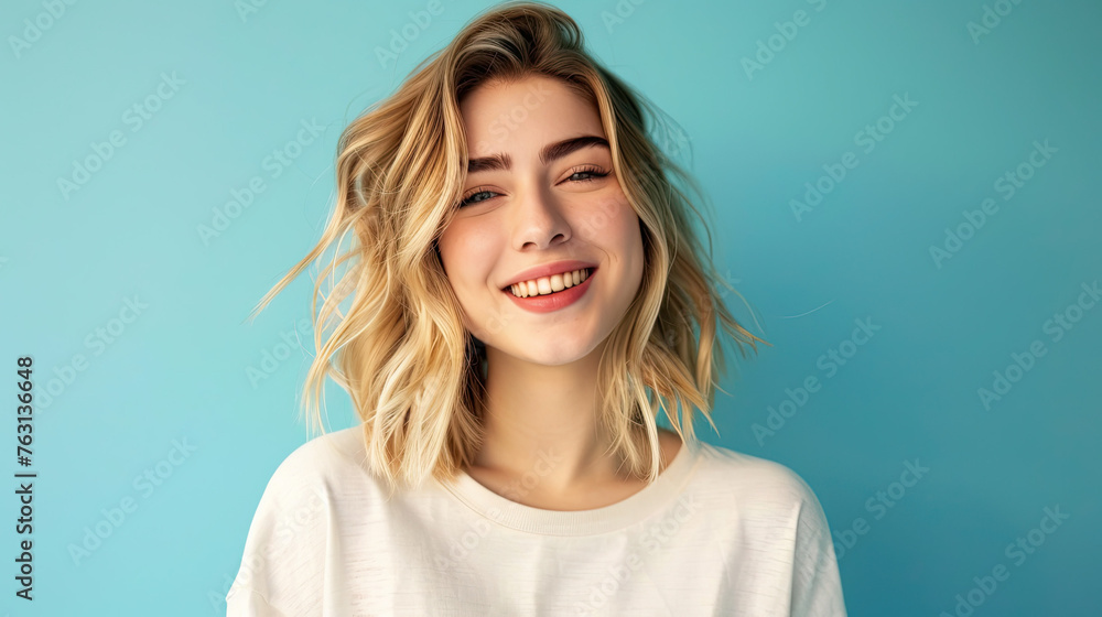 Pretty smiling joyfully female with fair hair, dressed casually, looking with satisfaction at camera, being happy on pastel blue background - obrazy, fototapety, plakaty 