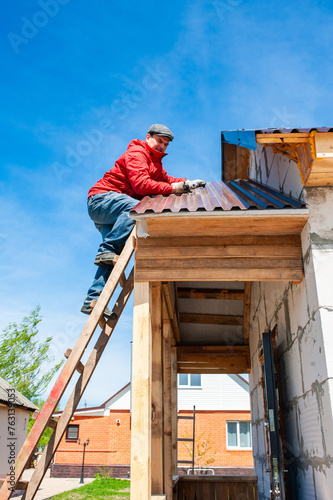 A worker builds a roof in a house while standing on a wooden ladder. Blue sky