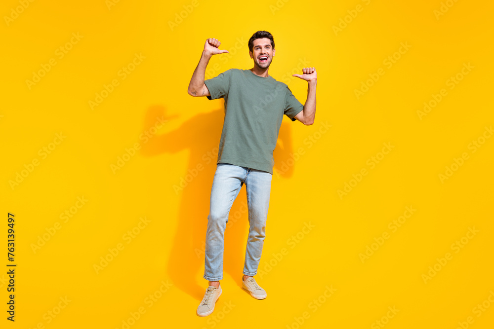 Full length photo of funky excited guy wear khaki t-shirt walking showing thumbs himself isolated yellow color background Full length photo of funky excited guy wear khaki t-shirt walking showing thumbs himself isolated yellow color background