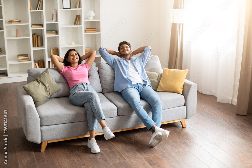 Relaxed indian spouses with hands behind head on the sofa