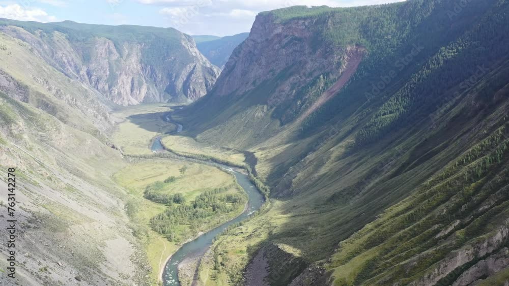 Flying over a narrow valley overgrown with forest between the mountains. A fast mountain river with amazing green water. River valleys. A winding river.