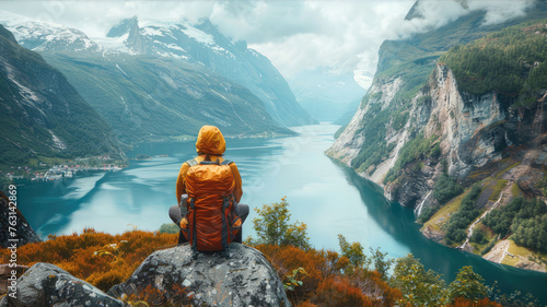 Traveler with backpack gazes at lake from rock in natural landscape