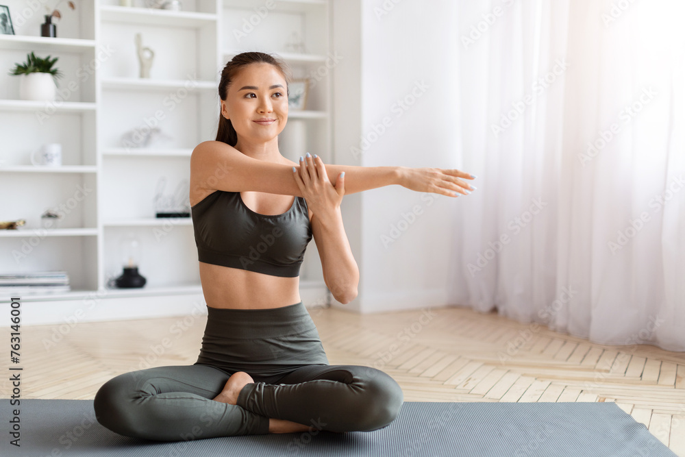 Smiling asian woman in yoga wear performing seated arm stretch exercise Smiling asian woman in yoga wear performing seated arm stretch exercise