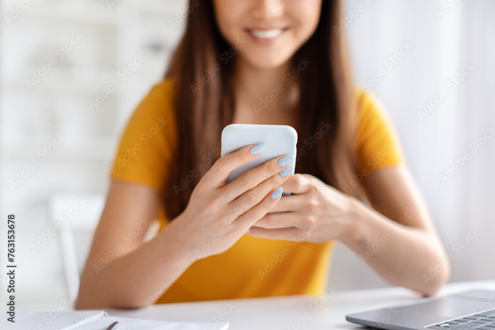 Smiling asian woman using her smartphone, texting or browsing internet at home Smiling asian woman using her smartphone, texting or browsing internet at home