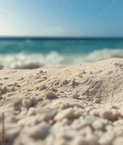 A close-up perspective shows the fine grains of sand on a sunlit beach, with the clear blue ocean extending towards the horizon under a clear sky