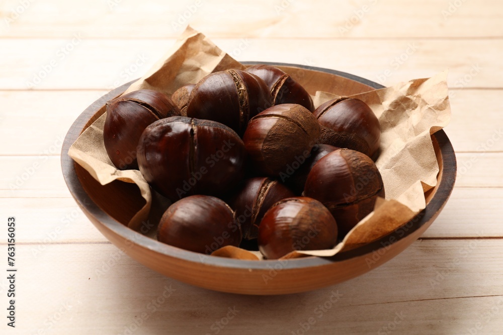 Roasted edible sweet chestnuts in bowl on wooden table, closeup Roasted edible sweet chestnuts in bowl on wooden table, closeup