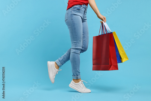 Woman with shopping bags on light blue background, closeup. Space for text