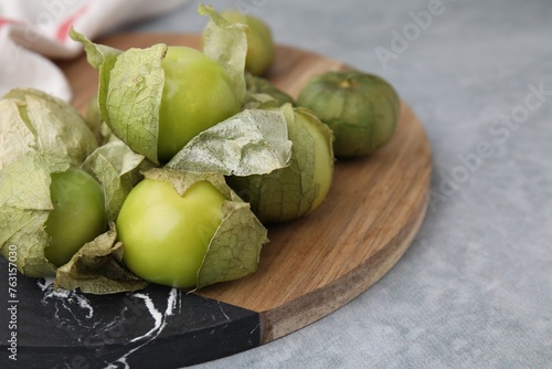 Fresh green tomatillos with husk on gray table, closeup photo