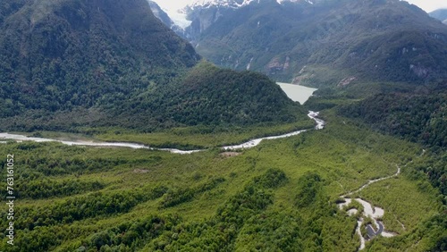 The camera pans up from the green forest to the glacier with waterfall and lake at Queulat National Park in Patagonia Chile snow-capped mountains and river photo