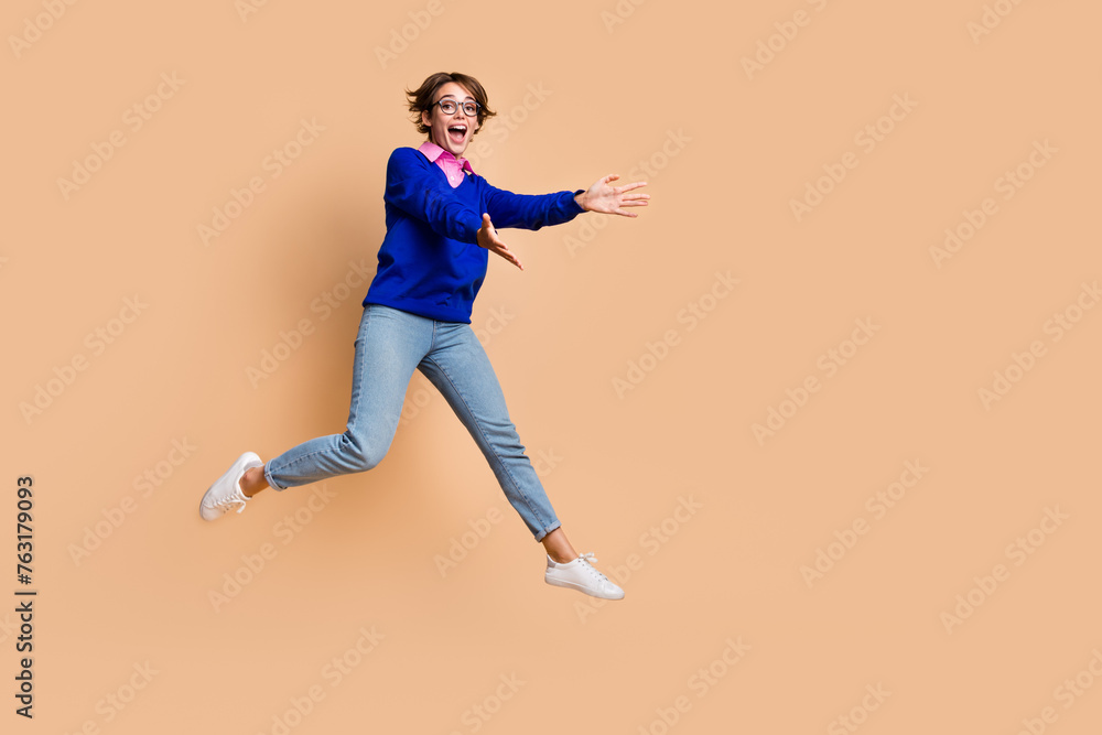 Full size portrait of astonished nice girl jump raise opened arms catch empty space isolated on beige color background