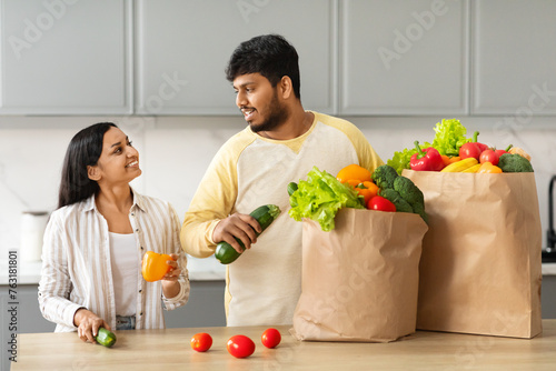 Happy Indian Couple Unpacking Bag With Groceries In Kitchen photo