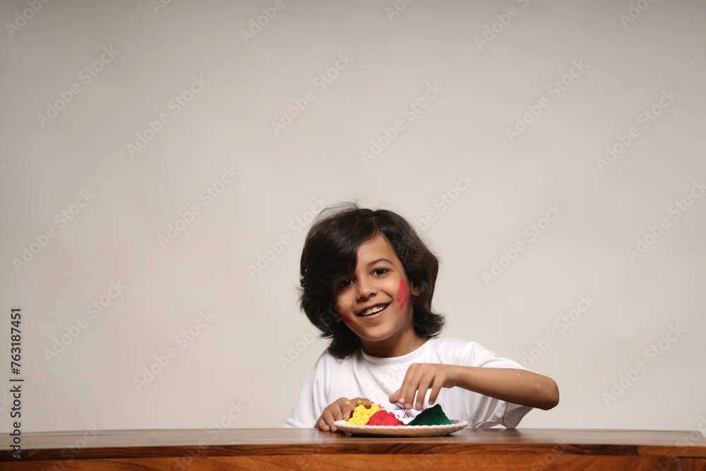 Young kid boy celebrating holi standing isolated on plain background Young kid boy celebrating holi standing isolated on plain background
