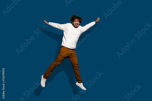 Full length photo of funky excited guy dressed white pullover jumping high empty space isolated dark blue color background