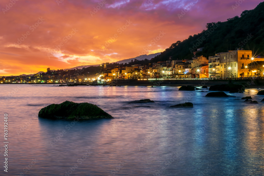 evening or night landscape of evening town coastline in golden lights and sea gulf with calm water and nice reflections with beautisul sunset sky on background