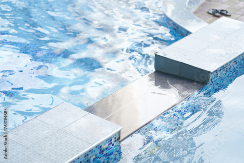 Part of swimming pool with blue mosaic ceramic tiles, with blue water, squared tiles, water surface, ripple. Background with copy space. Concept of summer, swimming, leisure time, vacation. © daryakomarova