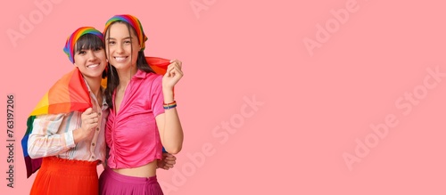 Young lesbian couple with LGBT flag on pink background with space for text