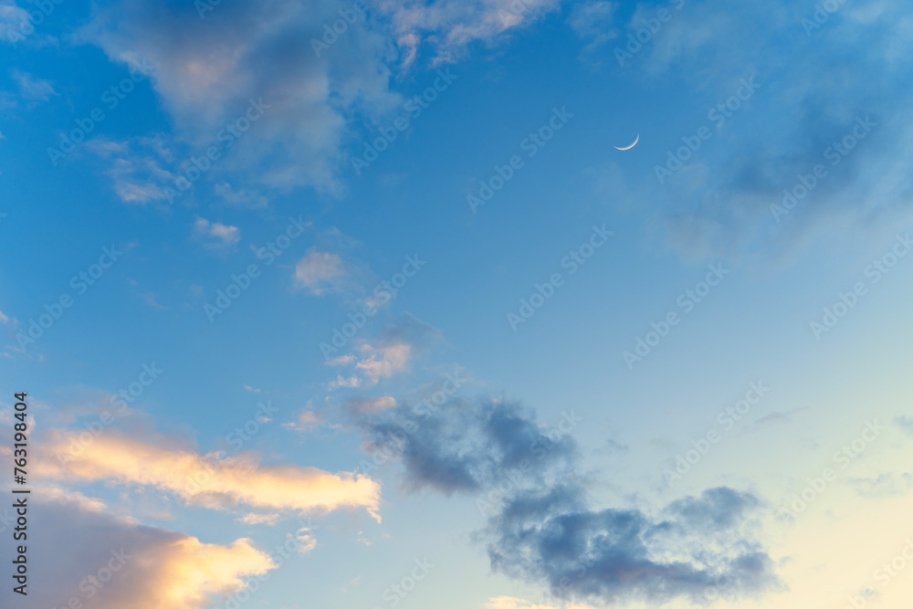 Gently blue sunset sky with pink clouds and moon disk, nature meteorology background