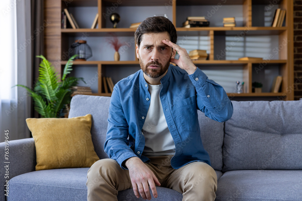 Worried man sitting on couch at home deep in thought