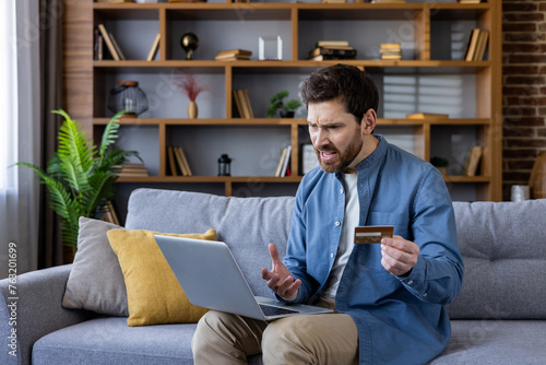 Frustrated man holding credit card looking at laptop