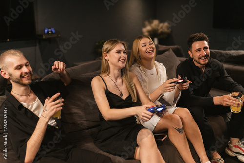 Happy men appreciate women players prowess in game room. Friends share in excitement of ladies gaming skills observing play with joy
