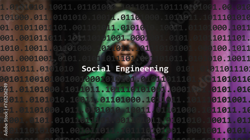 Social engineering cyber attack text in foreground screen, anonymous hacker hidden with hoodie in the blurred background. Vulnerability text in binary system code on editor program.
