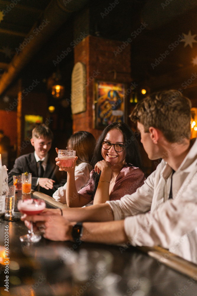 Pretty lady sits with young man at bar counter and smile. Double date at dinner with cocktails in romantic atmosphere in restaurant