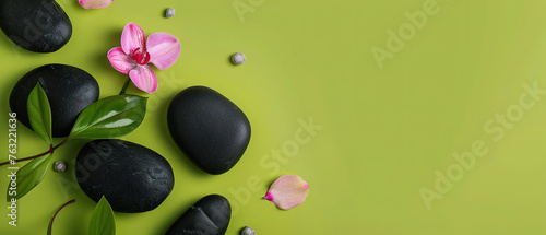 Flat lay composition with black spa stones and flowers isolated on green background with space for text 