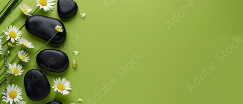 Flat lay composition with black spa stones and flowers isolated on green background with space for text 