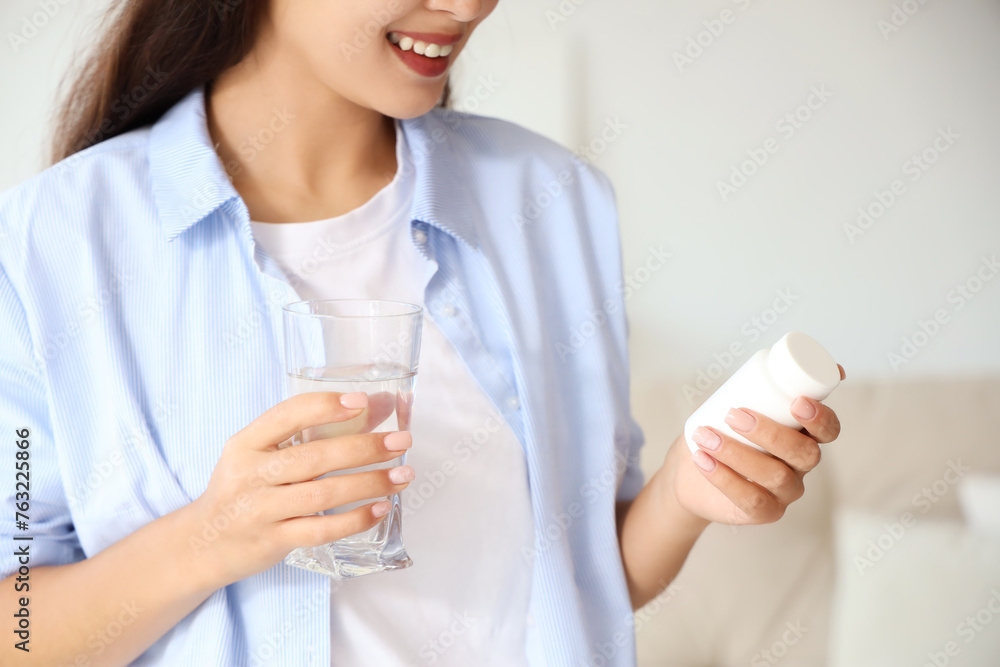 Young Asian woman with glass of water taking pills at home