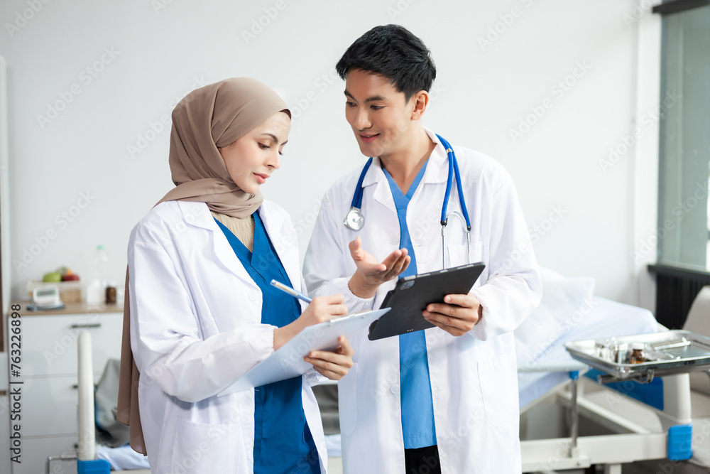 Hospital Ward. Doctor Talks With Professional Head Nurse or Surgeon, They Use Digital tablet Computer. Diverse Team of Health Care Hospital Ward. Doctor Talks With Professional Head Nurse or Surgeon, They Use Digital tablet Computer. Diverse Team of Health Care