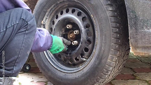 Kandra, Bashkortostan, Russia - December 01, 2023: Car mechanic removing car wheel covers using drill tool in service garage. photo