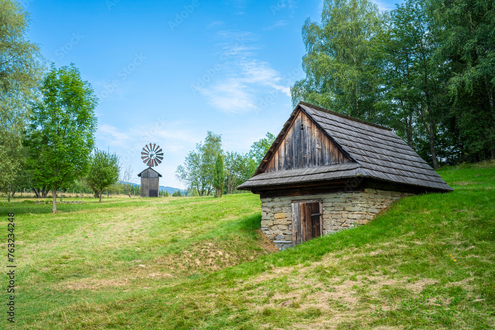 Old wooden windmill and Old wooden wallachia houses in old village with green meadow. Roznov pod Radhostem. Czech Republic.