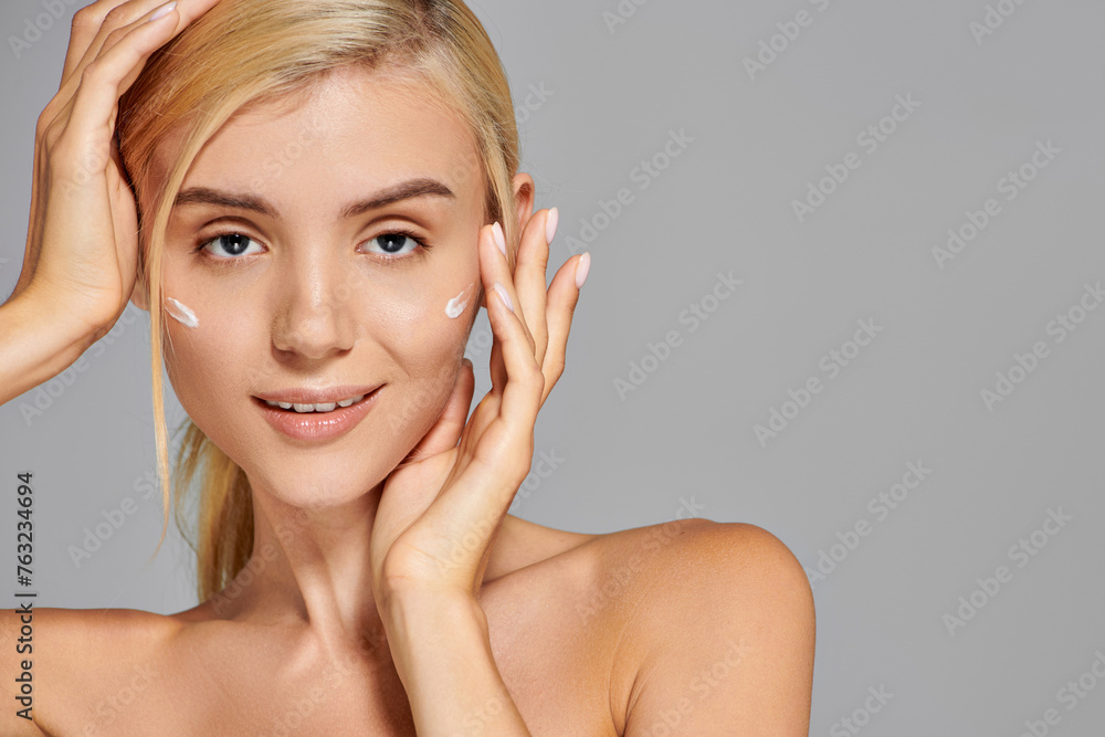 portrait charming blonde girl with her hands around head and cream on cheeks against grey background portrait charming blonde girl with her hands around head and cream on cheeks against grey background