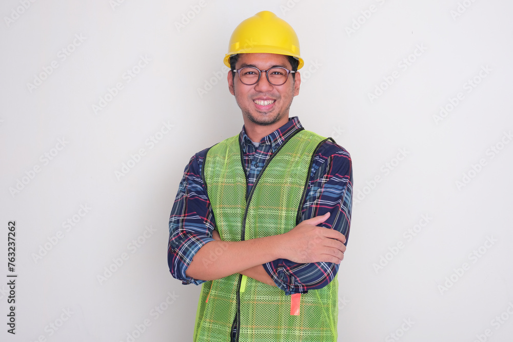 An engineer wearing hard hat and vest smiling with arms crossed An engineer wearing hard hat and vest smiling with arms crossed