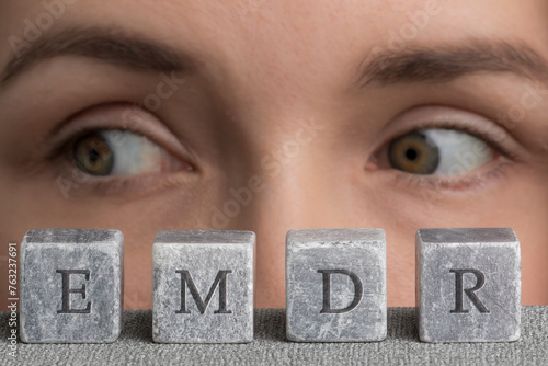 Eye Movement Desensitization and Reprocessing psychotherapy treatment concept. Letters EMDR written on grey stone cubes blocks. Close-up woman's face with eyes looking right.  photo