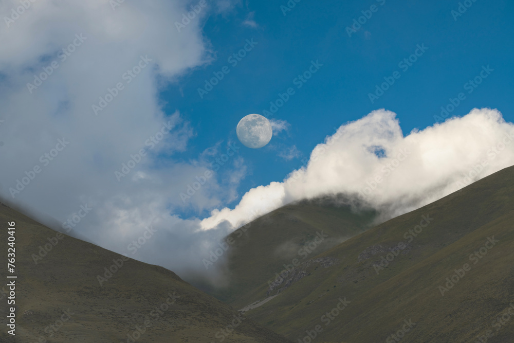 Beautiful mountains landscape with moon over the clouds.
